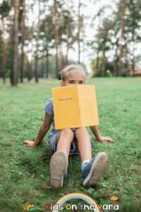 Back to school. Elementary school kid sitting on green grass with book at open-air class