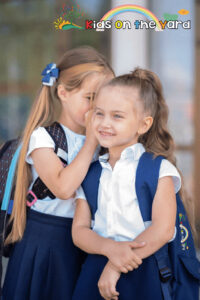 little girl schoolgirl tells a secret in her friend's ear